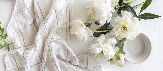 A summer themed flat lay with white peonies and a checkered linen plaid set on a white background featuring a healthy garden tea time picnic concept along with ample copy space for a text or image