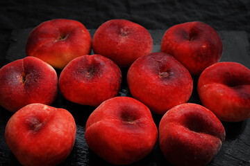 Ripe flat peaches on a black tray on a dark background