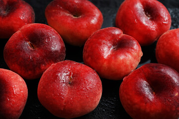 Ripe flat peaches on a black tray on a dark background