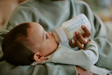 Medium close up of baby boy eating formula while his mother helping him with it