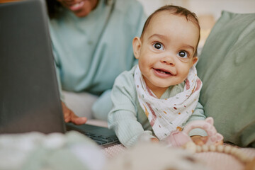 Baby boy wearing flax bib fooling around on comfortable bed while his mother working remotely via...