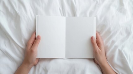 A person holds an open blank book on a soft white bed, inviting creativity and imagination in a serene environment.