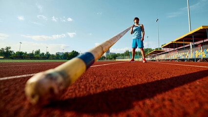Low angle view on male pole vault athlete in blue uniform standing at open air stadium with pole,...