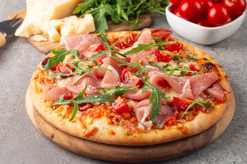 Pizza with prosciutto, ham, arugula, spinach, tomatoes, pesto, cheese and parmesan. Italian cuisine