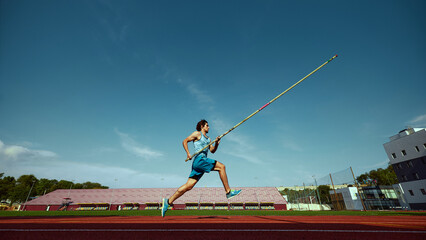 High jump training in progress, with a strong and focused pole vaulter in motion, running wit pole...