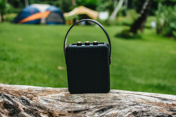 Black portable wireless speaker for listening to music on a log for camping.