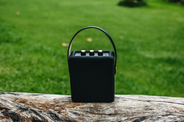 Black portable wireless speaker for listening to music on a log for camping.
