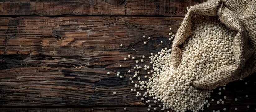Top view of spilled organic whole pearl millet or Bajra seeds from a jute bag with Bajra Flour on dark wood isolated background with copy space image