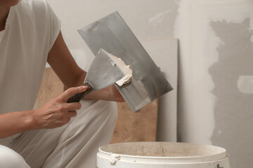 Woman taping and mudding joins pieces of drywall into a single solid wall. Fixing dry wall surface and preparation for painting. DIY housing improvement project.