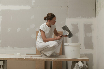 Woman taping and mudding joins pieces of drywall into a single solid wall. Fixing dry wall surface...