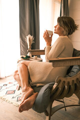 Beautiful young woman drinking tea or coffee in a cozy room in her home.