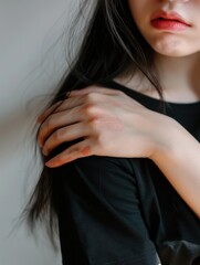 Obraz premium Asian woman wearing red lipstick, looking thoughtful or upset with hand on shoulder. Portrait taken from front.