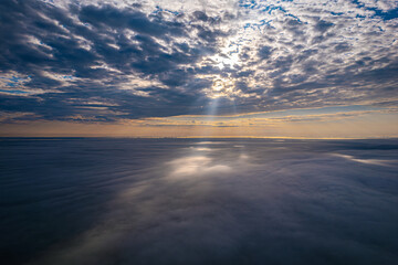 A stunning aerial view of a dramatic cloudscape with the sun's rays breaking through the clouds, casting a serene glow over the scene. The interplay of light and shadow creates a captivating and tranq