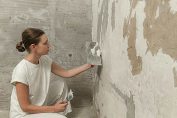 Woman plastering wall with putty-knife. Fixing wall surface and preparation for painting. DIY...