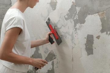 Woman plastering wall with putty-knife. Fixing wall surface and preparation for painting. DIY...