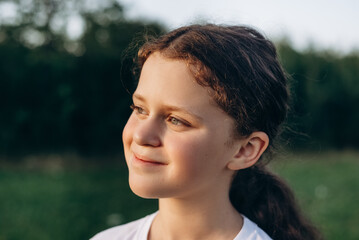 Portrait of smiling charming pretty little girl in park at summer warm day. Adorable happy child is dreaming looking at side on lawn outdoors. Children day. Childhood and nature concept