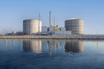 Obraz premium Nuclear Power Plant Reflections. A serene view of a nuclear power plant with its reflection in calm waters, showcasing the facility's architecture and the surrounding environment.