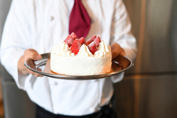 苺が乗ったショートクリームのホールケーキを持つ手元