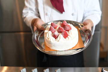 苺が乗ったショートクリームのホールケーキを持つ手元