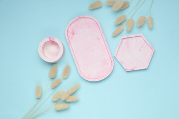 Set of Decorative pink plaster trays of different shapes on blue background with dried flowers.  Stands for candles organizers for cosmetics or jewelry. Top view