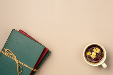 Stack of books with cup of herbal tea on a beige background. Leisure concept, reading a book. Copy space. Flat lay, top view