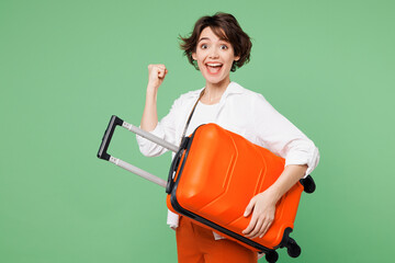 Traveler happy woman wear casual clothes hold orange suitcase bag do winner gesture isolated on...