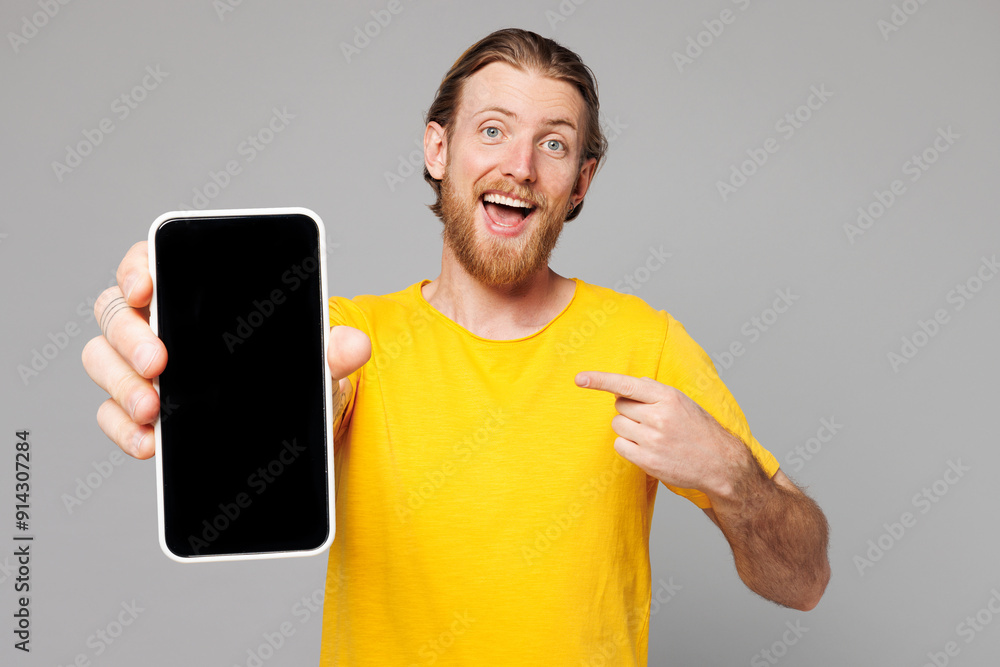 Sticker Young man he wear yellow t-shirt casual clothes hold in hand use point index finger on mobile cell phone with blank screen workspace area isolated on plain grey background studio. Lifestyle concept.