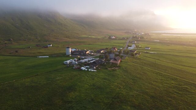 Farm buildings and fields under early morning mist and fog in Lofoten, Northern Norway by the Ryten mountain