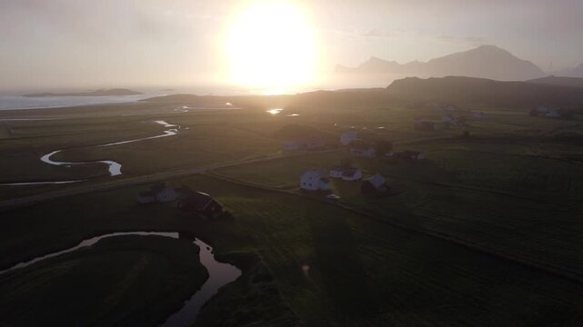 Farm buildings and fields under early morning mist and fog in Lofoten, Northern Norway by the Ryten mountain