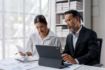 A man and a woman are sitting at a desk with a laptop and papers