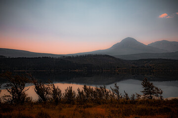 Landscape imageof the mountain silhouette reflecting in the lake, with a calm and misty sky. 