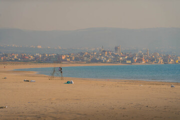 The empty Mediterranean sea beach with yellow sand, blue water and distant panorama of Tyre (Sour),...