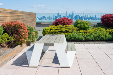 table with wooden top on a sunny terrace with bushy cedars and view over manhettan