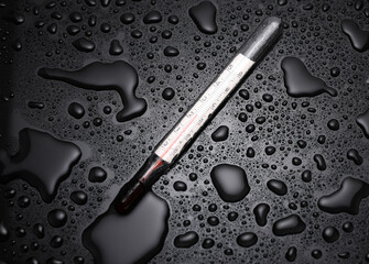 Thermometer on a black background with water drops