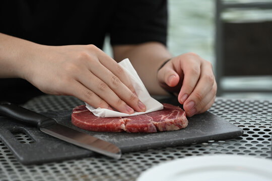 Drying Steak for a Perfect Cook, Hands gently patting down a raw steak to dry off with a paper towel on a cutting board