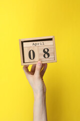 Wooden block calendar with date april 08 in hand on yellow background