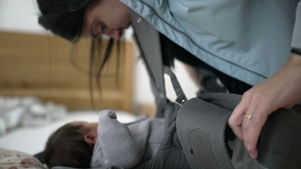 Mother adjusting baby carrier straps, securing newborn in gray knit sweater, intimate bonding moment, ensuring safety and comfort, parenthood, caring for baby, preparing for outing