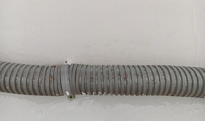 Fragment of big pipe pinned to the white cement (concrete) wall. Industrial. Technology. Object.  