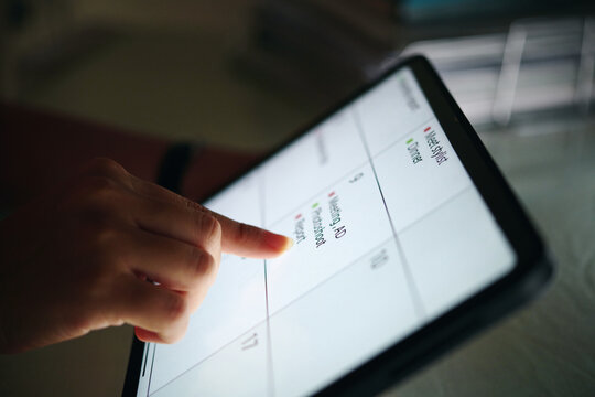 Hand pointing at digital calendar tablet, scheduling appointments and organizing events. Display showing dates, reminders, and tasks efficiently arranged