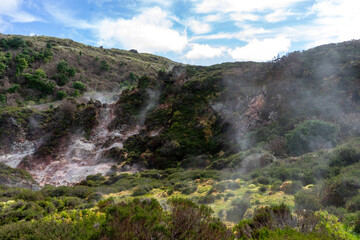 A dramatic volcanic landscape of steaming sulfur vents amidst lush greenery in Furnas do Enxofre, Terceira Island, Azores, Portugal. Nature's raw power captured in an ethereal, misty scene.