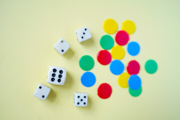White dices and colorful tokens on yellow background.	