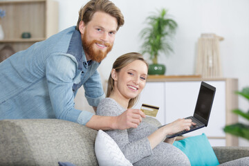 happy pregnant woman and man grinning and using laptop