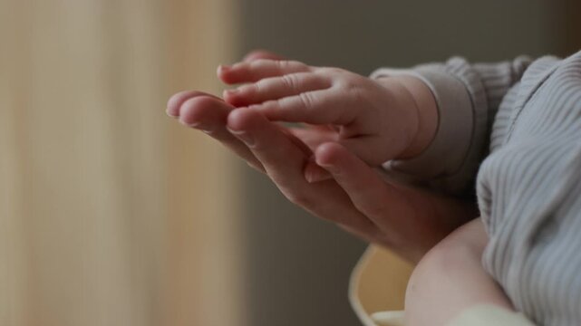 Extreme close-up of hand of unrecognizable woman gently touching tiny fingers and palm of baby feeling unconditional love and affection