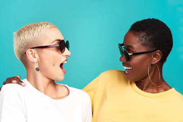 Women, wow and sunglasses with surprise, together and bonding on blue background as friends. Female people, shock and smile as cheerful in diversity, conversation and communication on studio backdrop
