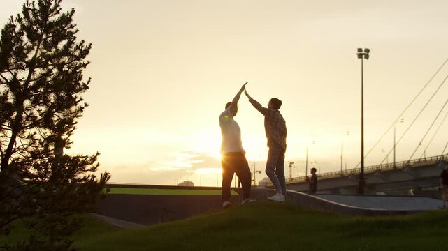Young man and a woman give each other high fives in the park, with the setting sun as a backdrop. Slow motion