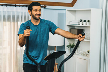 Athletic and sporty man running on elliptical running machine during home body workout exercise session for fit physique and healthy sport lifestyle at home. Gaiety home exercise workout training.