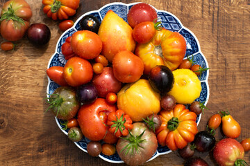 Many garden tomatoes in different colors, shapes and varieties on a blue rustic plate on a wooden table. Tomatoe composition with space for text.