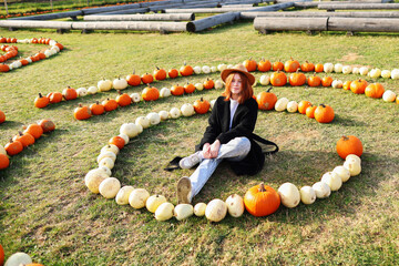 redhead girl looks at camera. She wears black coat and brawn hat. backdrop pumpkins. autumn season...