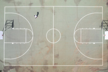 Direct overhead drone view of skateboarder on an empty basketball court on a sunny day