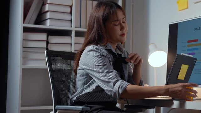 Busy office worker multitasking with laptop and charts, taking vitamins while working late. Desk lamp and sticky notes highlight a productive workspace